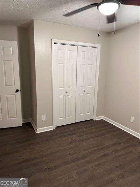 unfurnished bedroom featuring ceiling fan, dark hardwood / wood-style floors, a textured ceiling, and a closet