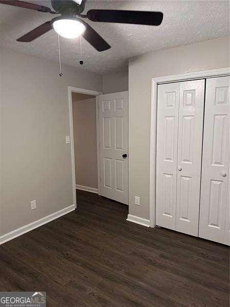 unfurnished bedroom featuring ceiling fan, dark hardwood / wood-style flooring, a textured ceiling, and a closet