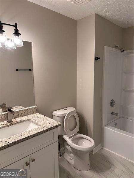 full bathroom featuring toilet, vanity, a textured ceiling, and bathtub / shower combination