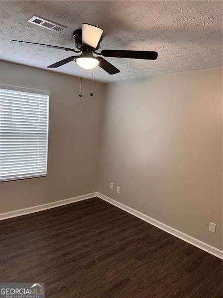 empty room with a textured ceiling, dark hardwood / wood-style floors, and ceiling fan