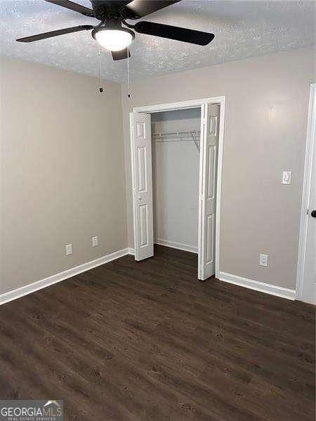 unfurnished bedroom with ceiling fan, a closet, dark wood-type flooring, and a textured ceiling