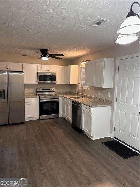 kitchen featuring sink, dark hardwood / wood-style flooring, light stone counters, white cabinetry, and stainless steel appliances