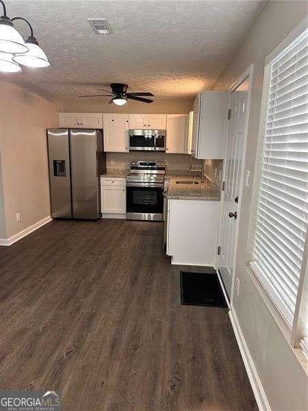 kitchen with hanging light fixtures, a textured ceiling, dark hardwood / wood-style flooring, white cabinetry, and stainless steel appliances