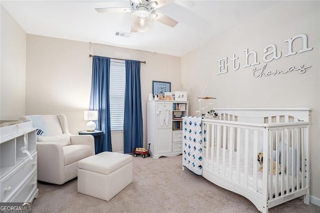 carpeted bedroom featuring ceiling fan and a nursery area