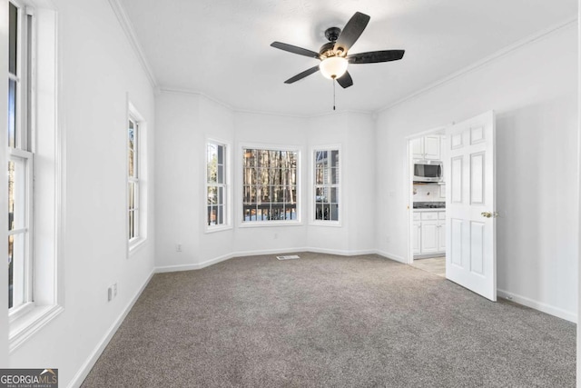 unfurnished living room featuring light carpet, a wealth of natural light, ceiling fan, and ornamental molding