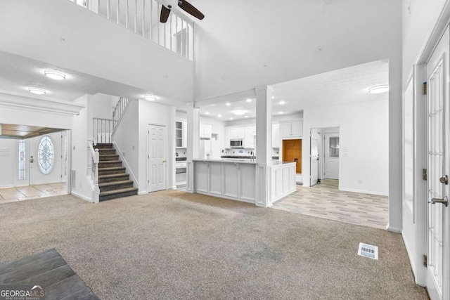 unfurnished living room with ceiling fan, a towering ceiling, and light carpet