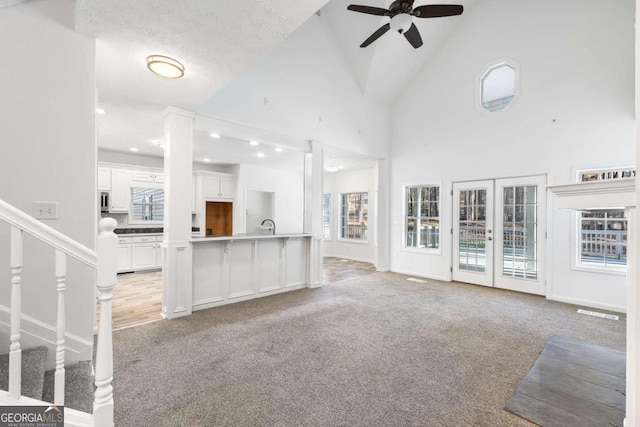 unfurnished living room featuring light carpet, high vaulted ceiling, ceiling fan, and plenty of natural light