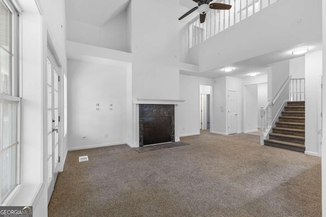 unfurnished living room featuring a tile fireplace, a towering ceiling, ceiling fan, and carpet flooring