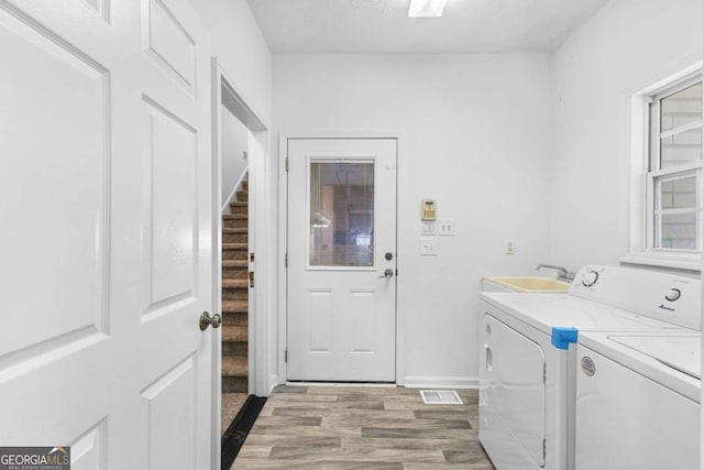 clothes washing area with washing machine and clothes dryer, sink, and hardwood / wood-style flooring