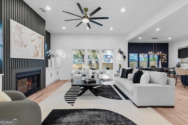 living room with ceiling fan with notable chandelier and light wood-type flooring