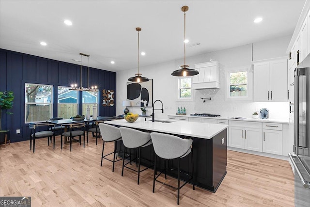 kitchen with sink, hanging light fixtures, a center island with sink, white cabinets, and light wood-type flooring