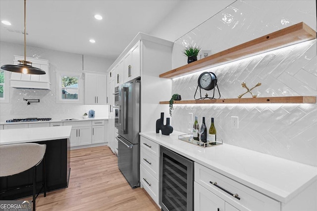 kitchen featuring decorative backsplash, appliances with stainless steel finishes, beverage cooler, white cabinetry, and hanging light fixtures