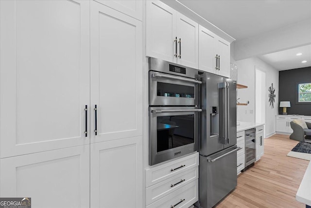 kitchen featuring white cabinetry, light hardwood / wood-style flooring, beverage cooler, and stainless steel appliances