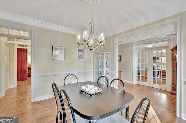 dining space with french doors, ornamental molding, light hardwood / wood-style floors, and a notable chandelier