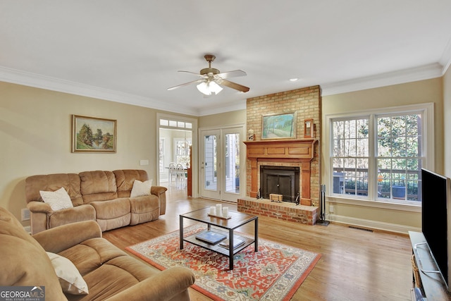 living room with a brick fireplace, crown molding, light hardwood / wood-style flooring, and ceiling fan