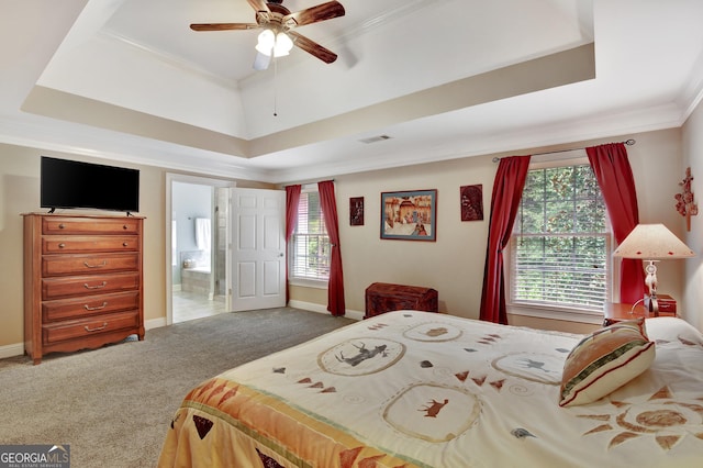 carpeted bedroom with a raised ceiling, crown molding, connected bathroom, and ceiling fan