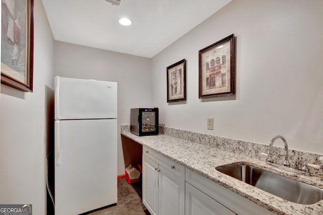 kitchen featuring white refrigerator, sink, light stone counters, and white cabinets