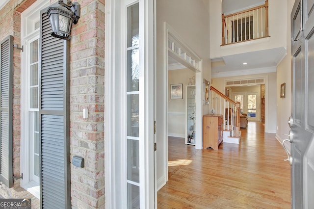 entrance foyer featuring ornamental molding, a towering ceiling, and light hardwood / wood-style floors