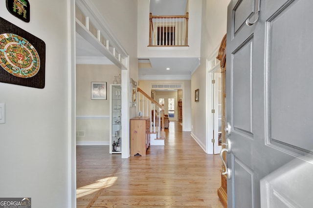 foyer with ornamental molding, a high ceiling, and light wood-type flooring