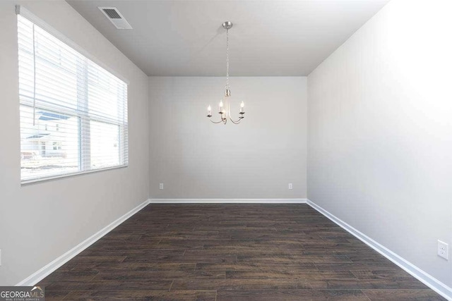 spare room featuring an inviting chandelier and dark wood-type flooring