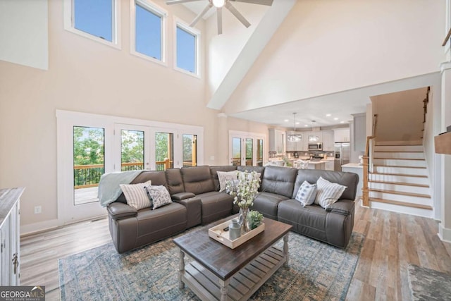 living room featuring ceiling fan, a high ceiling, and light hardwood / wood-style flooring