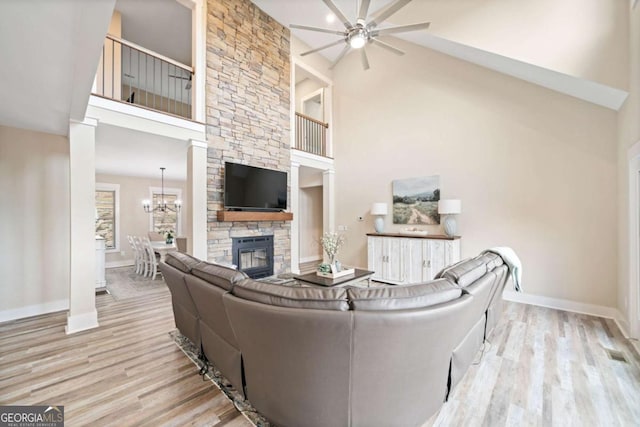 living room featuring ceiling fan with notable chandelier, light wood-type flooring, high vaulted ceiling, and a fireplace