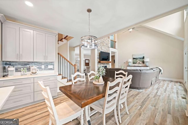 dining room with light wood-type flooring, ceiling fan with notable chandelier, and a stone fireplace