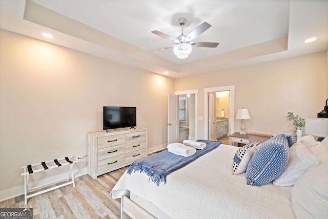 bedroom featuring ceiling fan, light hardwood / wood-style floors, ensuite bathroom, and a raised ceiling