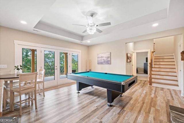 game room featuring pool table, french doors, light hardwood / wood-style floors, a raised ceiling, and ceiling fan