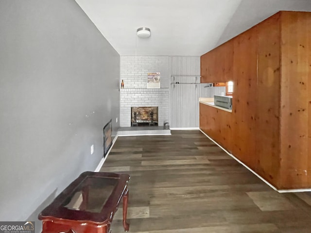 unfurnished living room featuring wood walls, dark hardwood / wood-style floors, and a brick fireplace