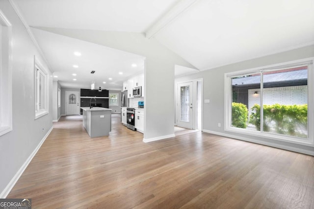 unfurnished living room featuring sink, lofted ceiling with beams, and light wood-type flooring