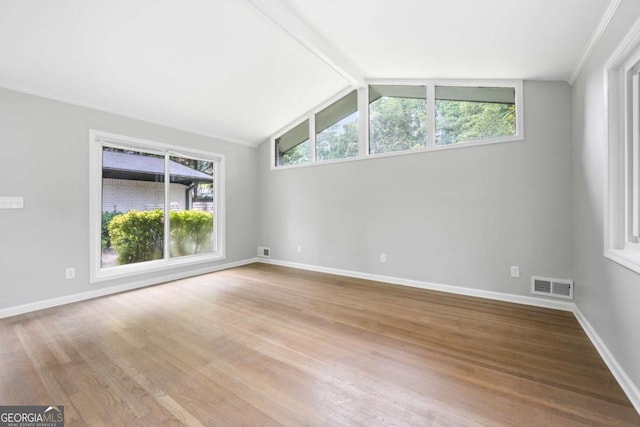 empty room with a wealth of natural light, lofted ceiling with beams, and light hardwood / wood-style floors