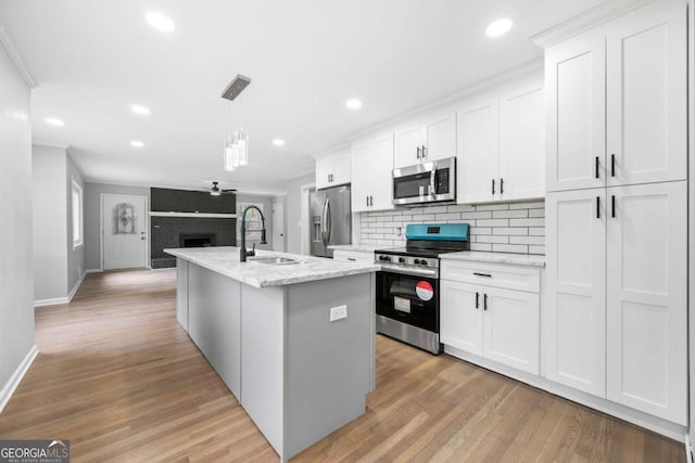 kitchen with pendant lighting, a center island with sink, sink, white cabinetry, and stainless steel appliances