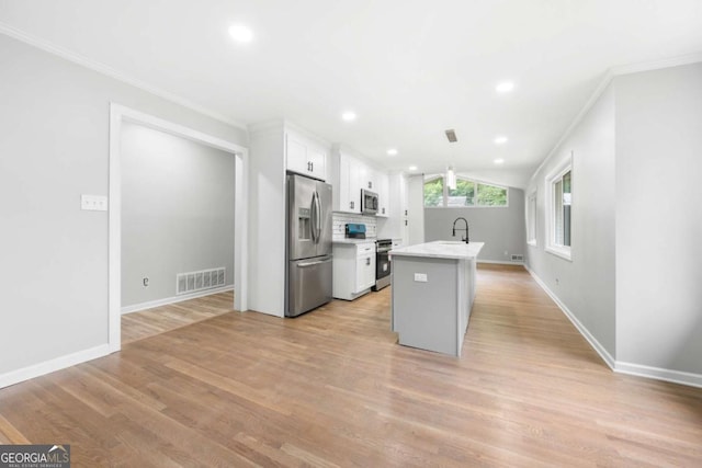 kitchen with appliances with stainless steel finishes, a kitchen island with sink, sink, pendant lighting, and white cabinetry