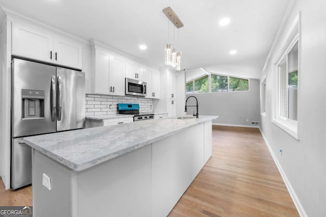 kitchen with appliances with stainless steel finishes, a center island with sink, white cabinetry, and hanging light fixtures