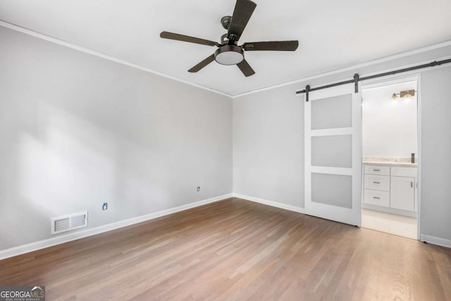 unfurnished bedroom featuring ensuite bathroom, light hardwood / wood-style flooring, ceiling fan, a barn door, and ornamental molding