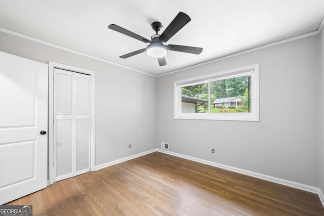 unfurnished bedroom featuring hardwood / wood-style floors, a closet, ceiling fan, and crown molding