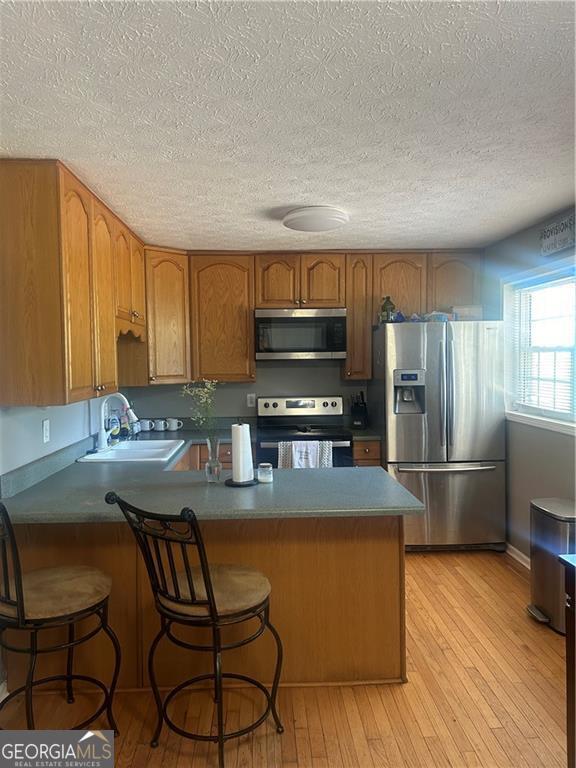 kitchen with a breakfast bar, sink, appliances with stainless steel finishes, light hardwood / wood-style floors, and kitchen peninsula