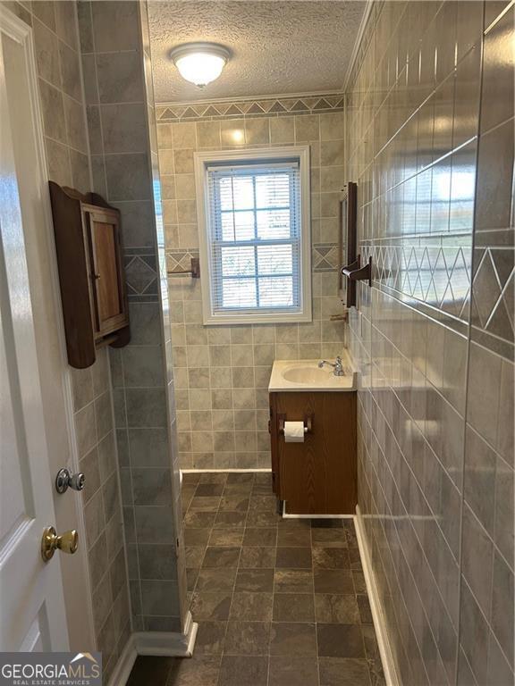 bathroom with a textured ceiling, vanity, tile walls, and walk in shower