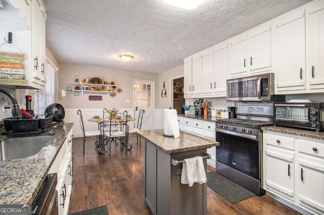 kitchen with white cabinetry, a center island, sink, stainless steel appliances, and dark stone counters