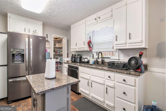 kitchen with white cabinets, stainless steel appliances, a kitchen island, and dark stone counters