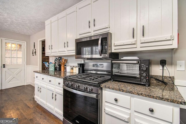 kitchen with white cabinets, a textured ceiling, appliances with stainless steel finishes, and dark stone counters