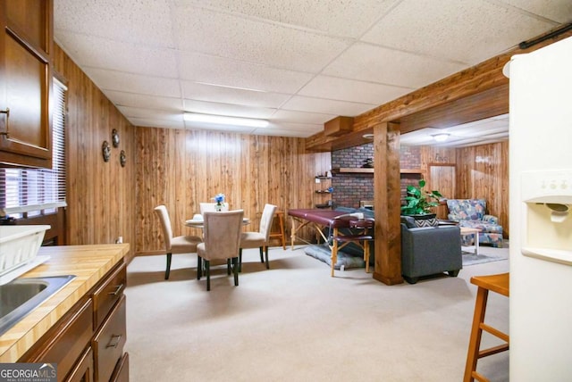 carpeted dining room with a drop ceiling, sink, and wooden walls