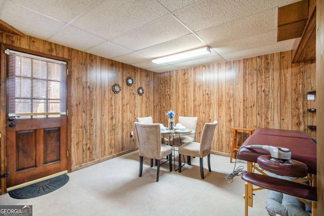 dining room with a paneled ceiling, carpet, and wooden walls