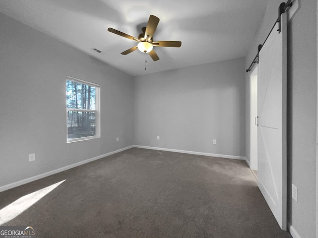 unfurnished bedroom featuring ceiling fan, a barn door, and dark carpet