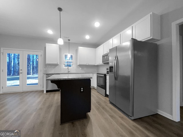 kitchen with hanging light fixtures, appliances with stainless steel finishes, a kitchen island, light stone counters, and white cabinetry