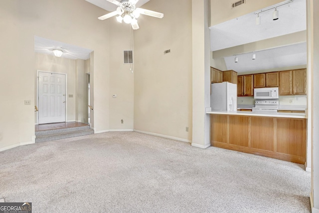 unfurnished living room featuring a high ceiling, light carpet, track lighting, and ceiling fan