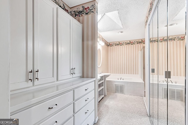 bathroom with a relaxing tiled tub and a textured ceiling