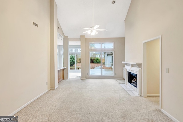 unfurnished living room featuring light carpet, a towering ceiling, a fireplace, and ceiling fan