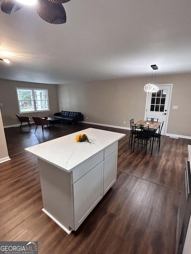 kitchen featuring pendant lighting, dark hardwood / wood-style floors, a kitchen island, light stone counters, and white cabinetry